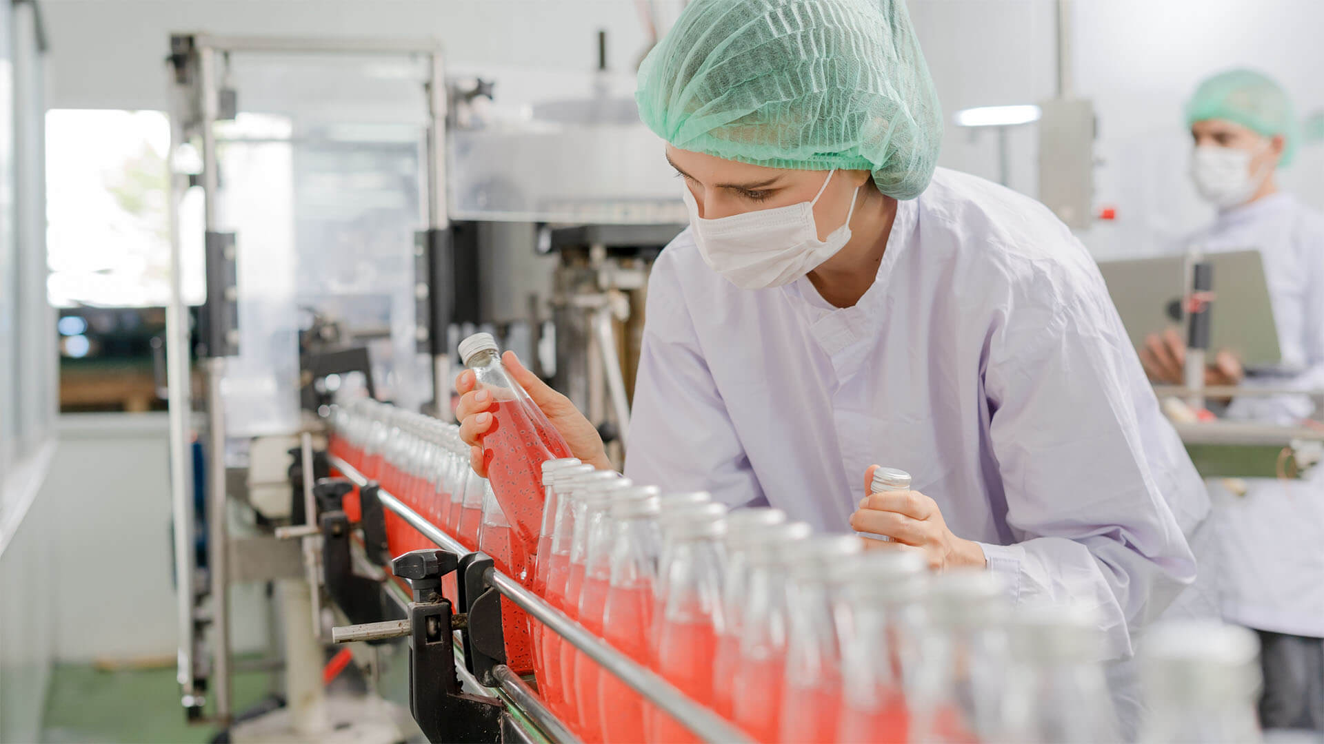 Woman doing a quality control check on bottled drink on an assembly line